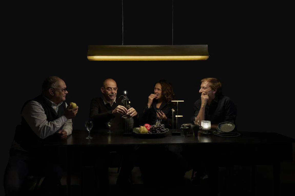 DCW Editions Respiro black and gold linear pendant illuminating 4 people sat a black table with wireless table lamps