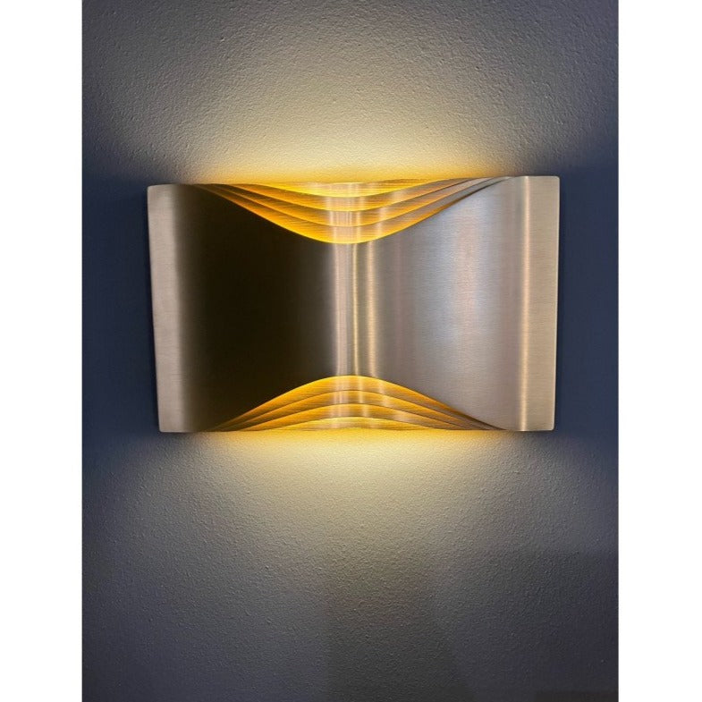DCW Editions Respiro brass wall light with curved brass metal lit on grey background