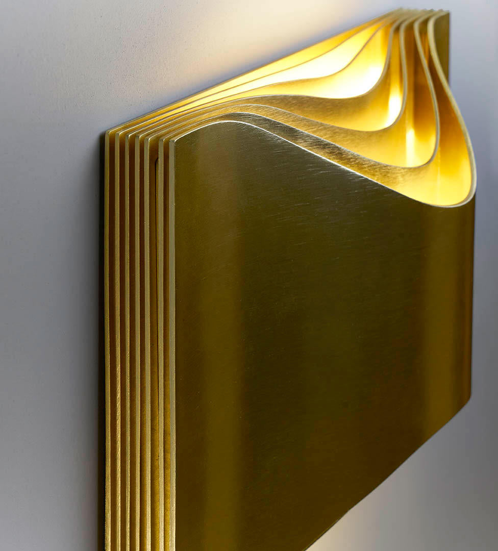 DCW Editions Respiro brass wall light with curved brass metal lit from the centre