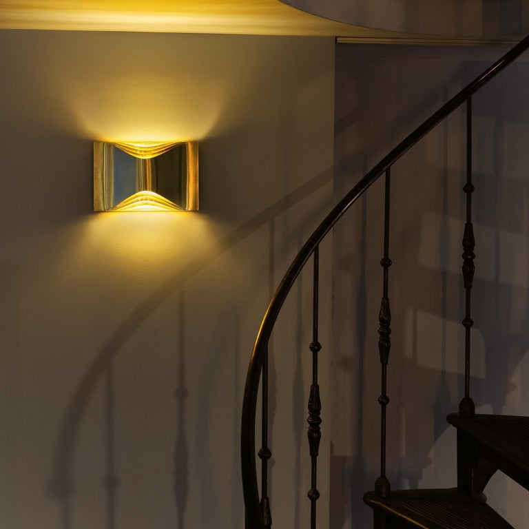 DCW Editions Respiro brass wall light with curved brass metal illuminated by black spiral staircase