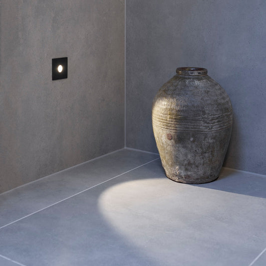 Astro Tango step light in black casting a beam of light onto the floor and a near by vase