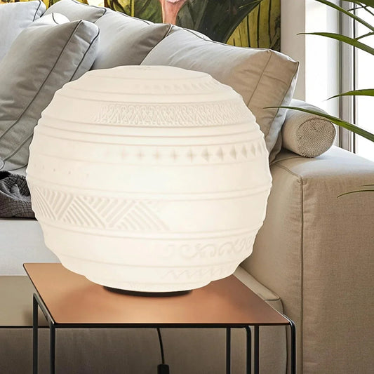 White textured table lamp on a wooden side table with a beige sofa and plant in the background